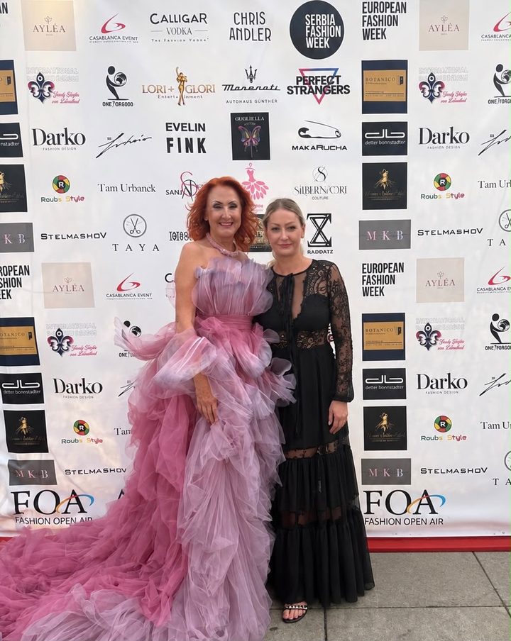Marietta in der rosa Tüllrobe mit Jona Hoffmann von Silbernadel Couture vor der Sponsorenwand der FOA Fashion Week Berlin