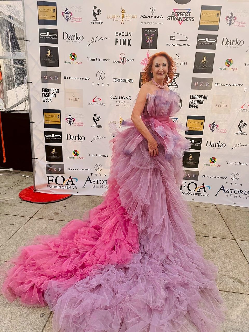 Marietta vor der Sponsorenwand der FOA Fashion Week, die Schleppe der Tüllrobe seitlich ausgebreitet