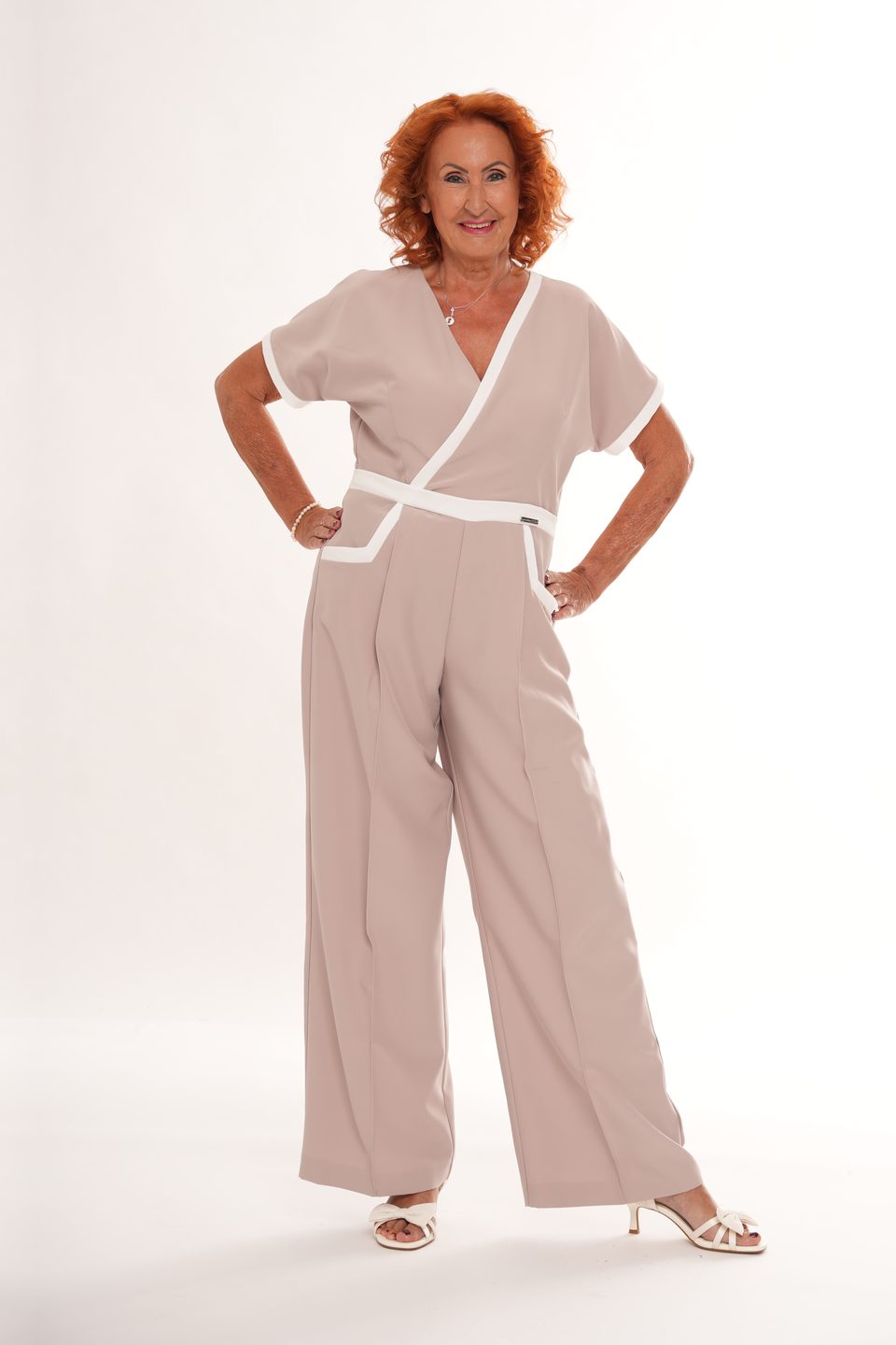 Marietta im hellen Jumpsuit, Hände in der Hüfte, aufrechte Haltung